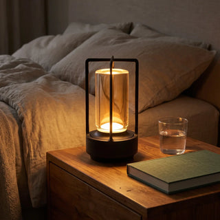 Morven Lantern cordless lamp lit on a bedside table beside a bed at night