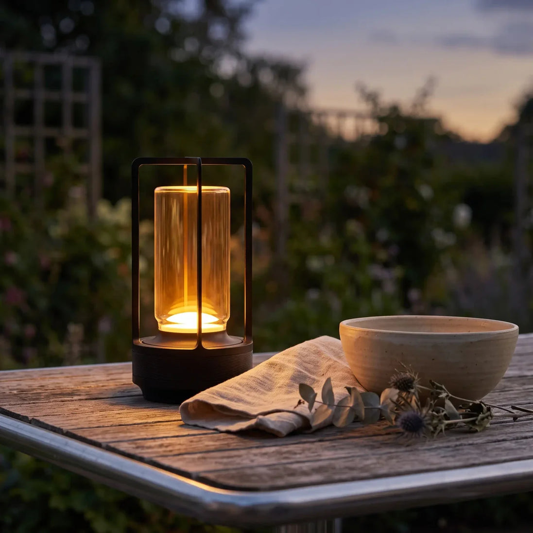 Morven Lantern cordless lamp lit on an outdoor wooden table at dusk