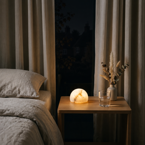 Morven Opaline alabaster lamp lit on a bedside table beside a bed