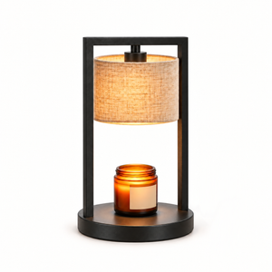 Morven Scrim candle warmer lamp with a cream linen shade, lit, on a plain background